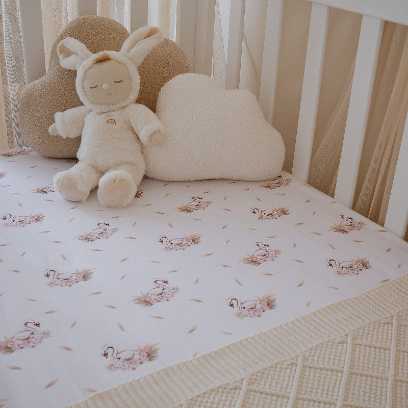 Adorable plush toy sitting in the conner of a cot set with a swan printed fitted cot sheet from snuggly jacks Australia.