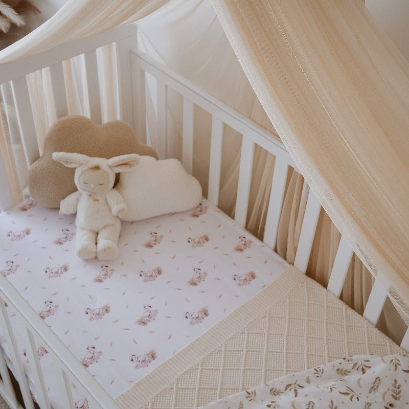 White pine cot set with swan printed linen, a cream knitted blanket and several plush toys in the top corner