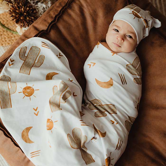 Baby laying on a pillow wearing a Snuggly Jacks Jersey Swaddle wrap and matching knotted beanie