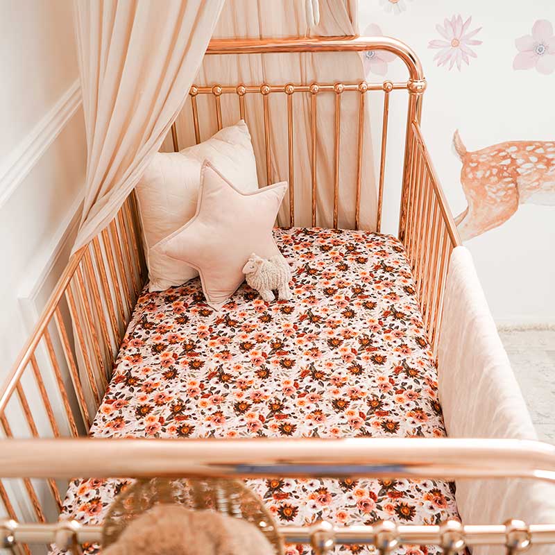 Baby girls nursery with a rose gold cot featuring a Snuggly Jacks Blithe Fitted Cot Sheet and 2 throw cushions.