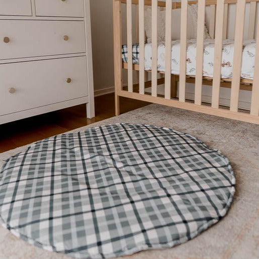 A cotton playmat on the floor of a nursery with a pine cot and a white chest of draws in the background