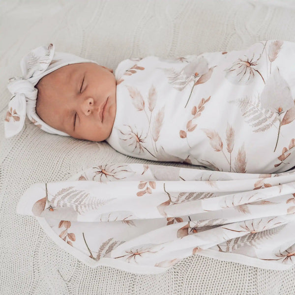 Adorable baby in white floral stretch wrap. This can help when wondering how to swaddle your baby. Tie a top knot.