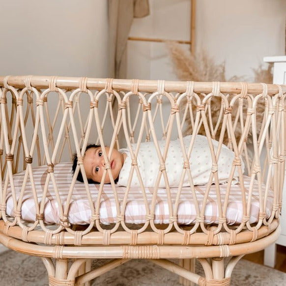 Beautiful baby laying in a Rattan bassinet set with a brown plaid cotton sheet