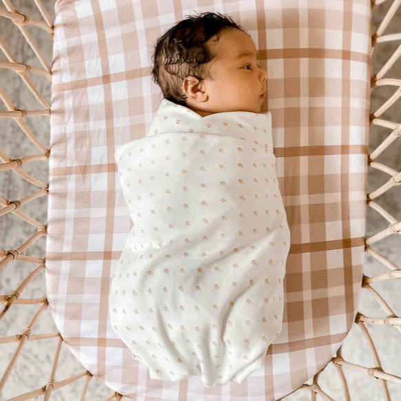 Close over head shot of a dark haired baby lying in a bassinet set with a brown plaid snuggly jacks sheet