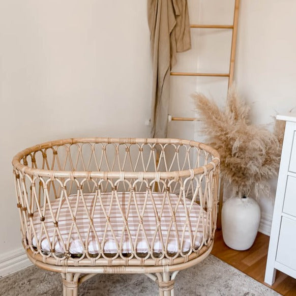 Modern Boho nursery with a rattan bassinet, decrotive bamboo ladder in the back ground, a vase with decorative grass and a  white chest of draws on the very right side of the space.