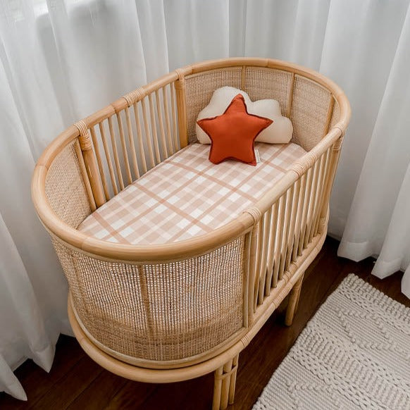 Rattan bassinet in the corner of a room with soft defused light helping show off the soft browns of a cotton bassinet sheet and a star pillow.