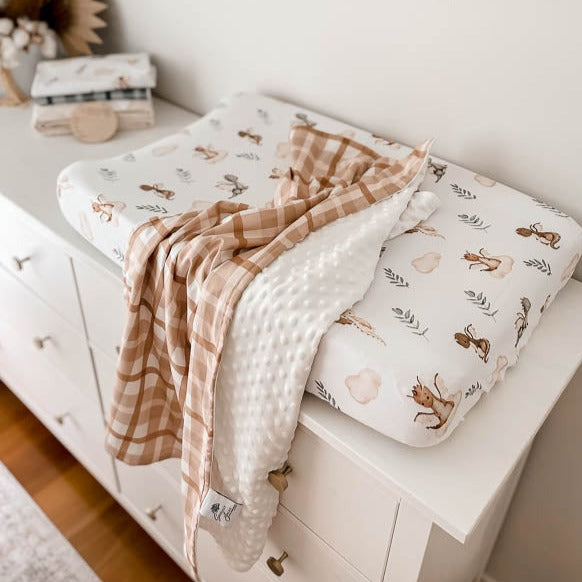 A high perspective of a minky pram blanket draped over a change table in a modern nursery setting.