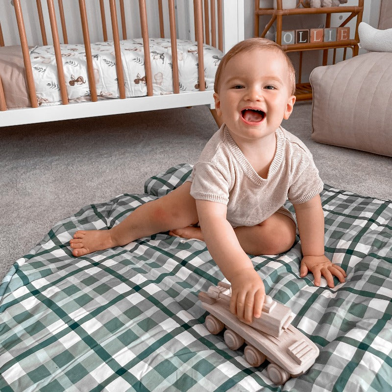 A toddler playing with a wodden tank on a cotton play mat
