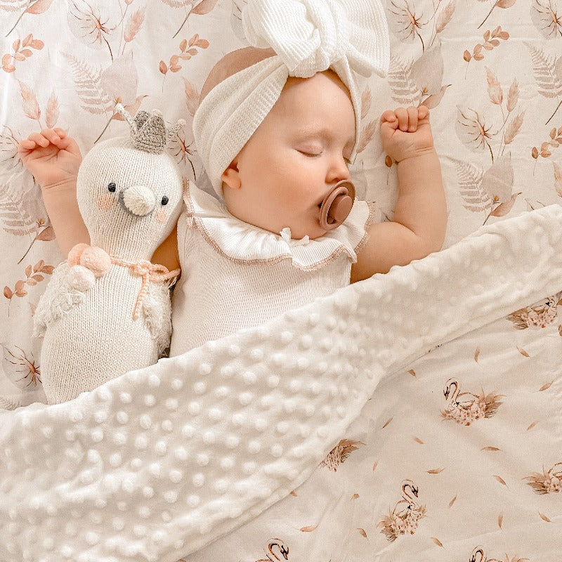 Adorable baby sleeping on a pattern with pastel coloured leaves with a dimple dot minky blanket laying over her and her plush toy.