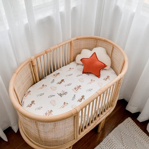 Bassinet in the corner of a modern room with soft white light bringing out the soft browns and greens found on the bassinet sheet