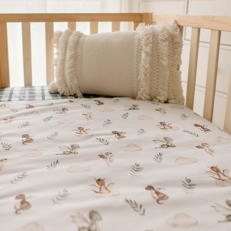 A low angel shot of a cot quilt with dragon prints and a tasselled pillow in the background
