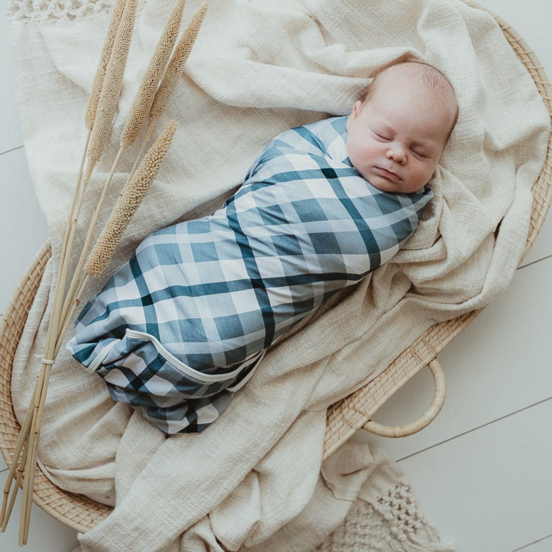 Adorable baby wrapped in a blue plaid wrap laying on top of a cotton blanket in a moses basket