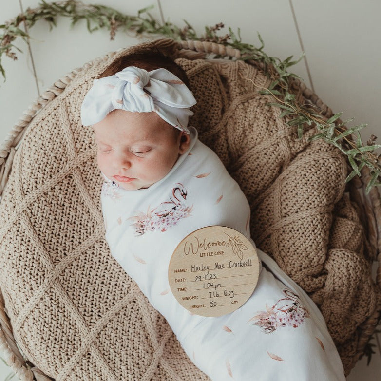 Bright white light cascading in on a cute baby swaddled and laying on a soft cotton knitted blanket using an announcement disk to show when she was born.