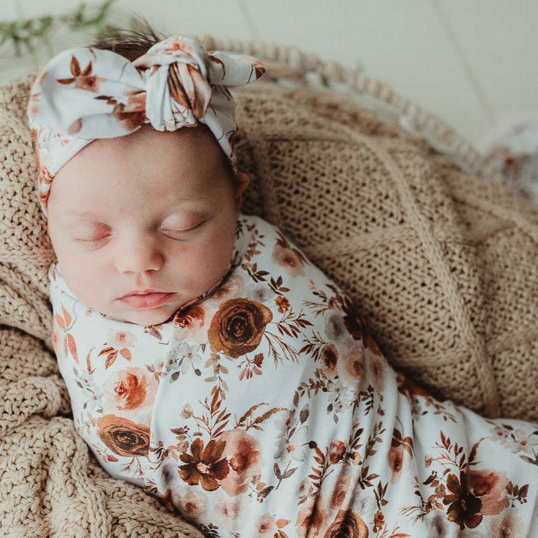Close up of a sleeping baby wearing a floral jersey top knot and wrapped in a swaddle