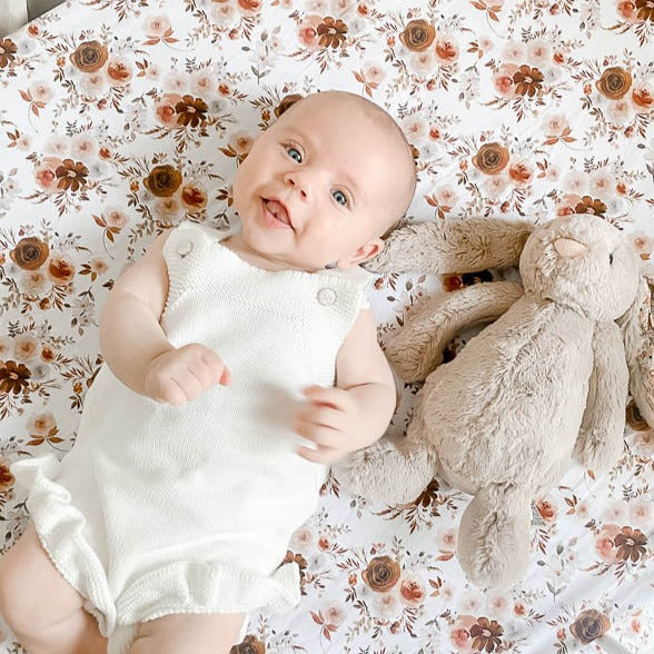 Sweet blue eyed baby laying beside a stuffed bunny on a fitted cot sheet