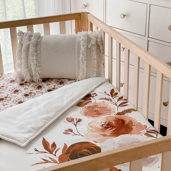Pine cot from an angel showcasing a large print floral cotton quilt with a tasselled pillow resting in the corner