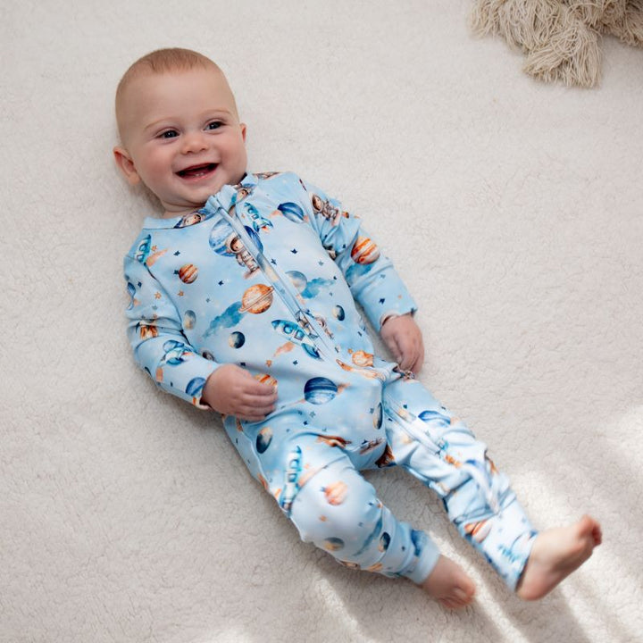 Baby lying on a soft surface, smiling while wearing a Space Rockets organic cotton onesie, featuring spacemen and planets for a vibrant nursery look.