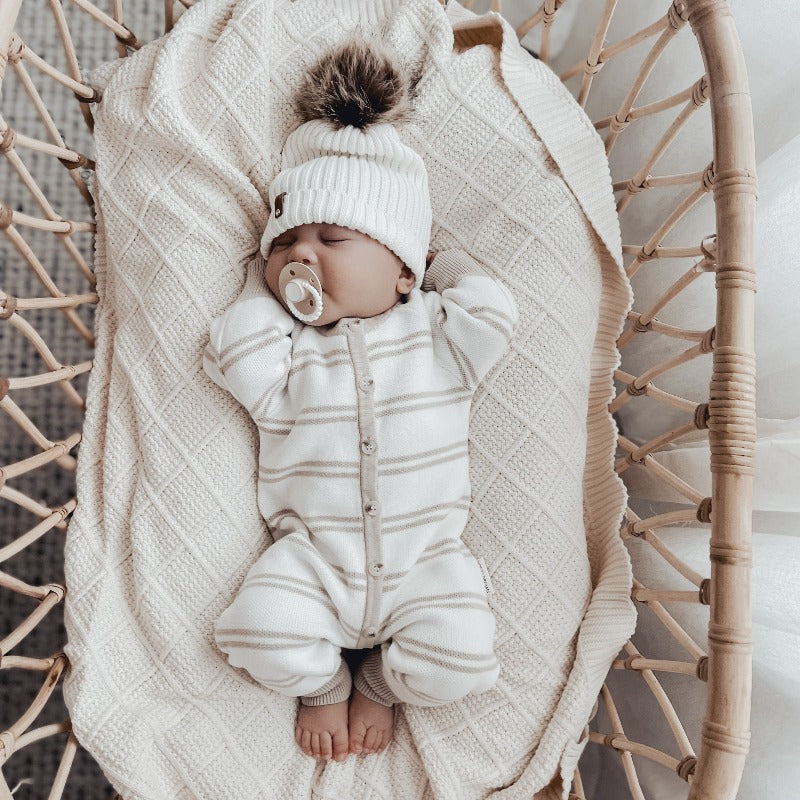 A soft and warm cotton knitted blanket in cream color from Snuggly Jacks, a premium Australian brand of knitted blankets and throws, placed in a bassinet