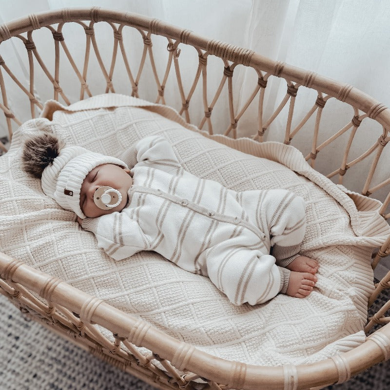 A large and luxurious cream knitted blanket made of cotton by Snuggly Jacks, used as a bassinet cover
