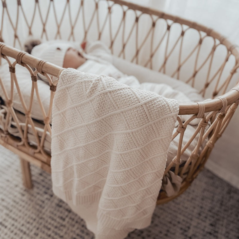 Cosy cream knitted blanket draped over the side of a ratan bassinet
