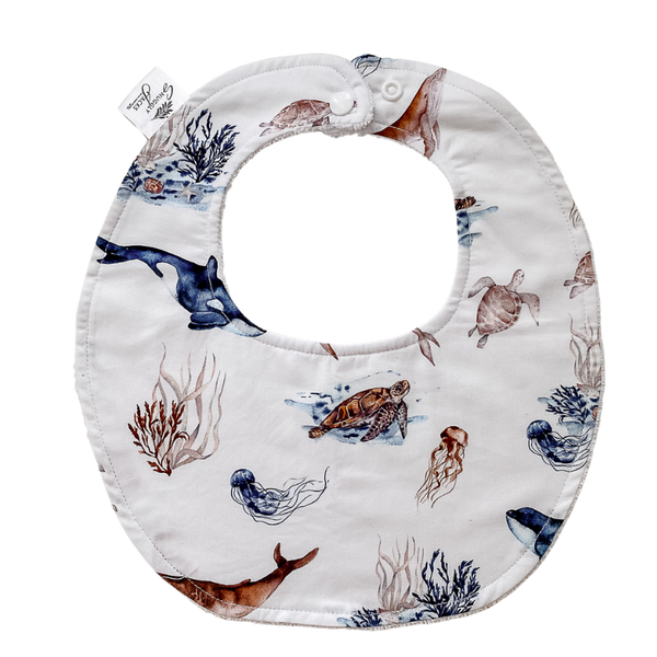 Flat lay of an organic cotton ocean-themed baby bib featuring a vibrant marine animal print, super absorbent backing, and adjustable snaps for a perfect fit.