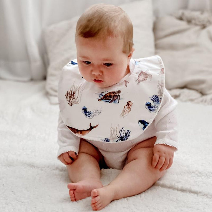 Baby wearing an ocean-themed organic cotton bib with marine animals like turtles and whales, showcasing the bib's soft and absorbent design for mess-free mealtimes.