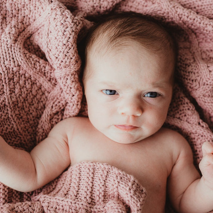 A soft and cozy rose pink cotton knitted blanket by Snuggly Jacks, wrapped around an adorable baby