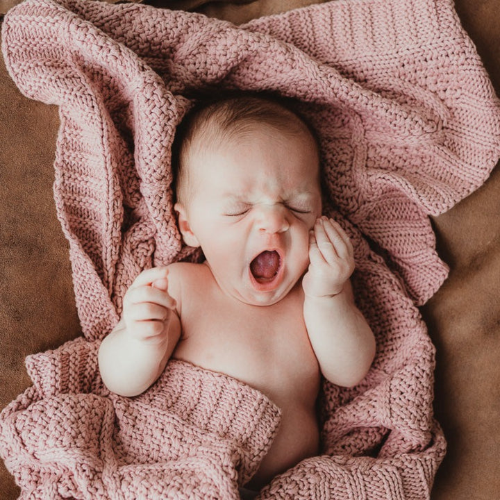 A large and soft rose pink knitted blanket made of cotton by Snuggly Jacks, used by a charming baby