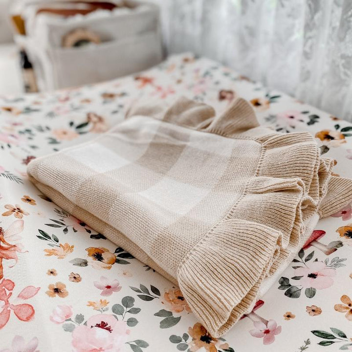 Sand gingham frill baby blanket placed on floral nursery bedding, showcasing soft organic cotton and stylish design.