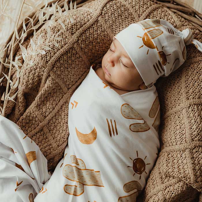 Baby sleeping  wrapped in a stretch jersey swaddle with a knotted beanie