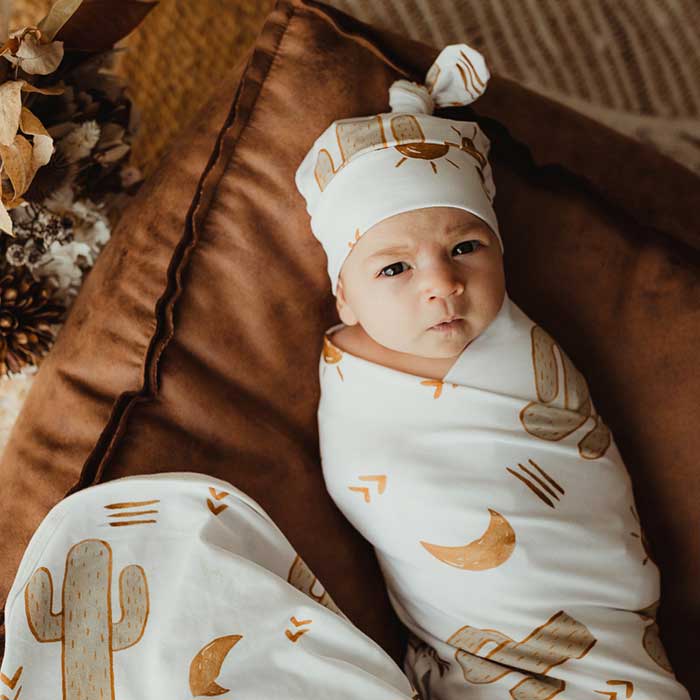 Baby with big brown eyes wearing a snuggly jacks jersey swaddle wrap and a matching knot beanie