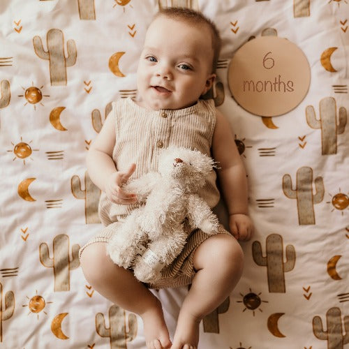 6 month old baby boy laying on a Snuggly Jacks Arizona fitted cot sheet holding his stuffed bear 