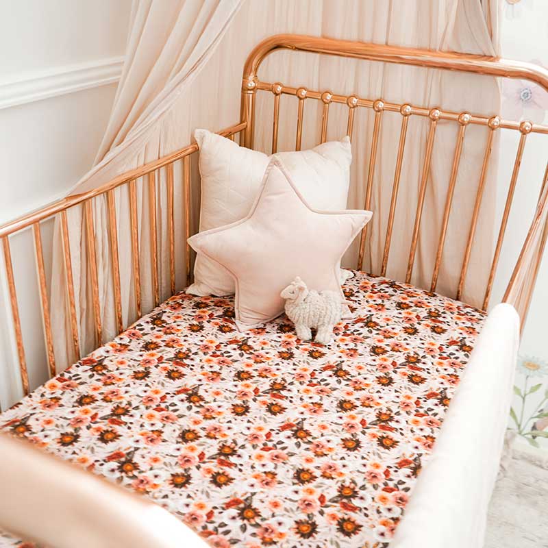 Baby girls nursery with a rose gold cot featuring a Snuggly Jacks Blithe Fitted Cot Sheet and 2 throw cushions.