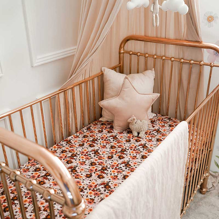 Baby girls nursery with a rose gold cot featuring a Snuggly Jacks Blithe Fitted Cot Sheet and 2 throw cushions.