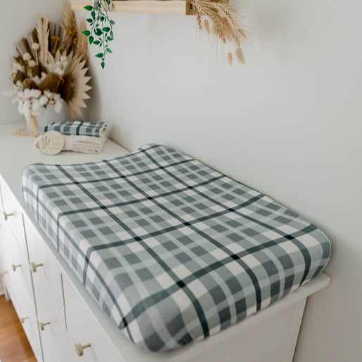Blue plaid cotton bassinet sheet set out on a white pine chest of draws with a matching burp cloth in the background