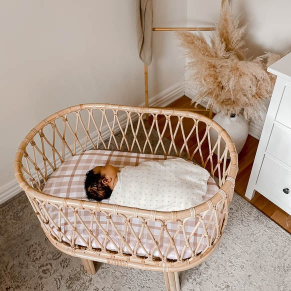 Adorable dark haired baby sleeping in a bassinet set with a cotton bassinet sheet.