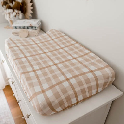 Change table mat covered with a brown plaid cover and set on a table with burp cloths in the background
