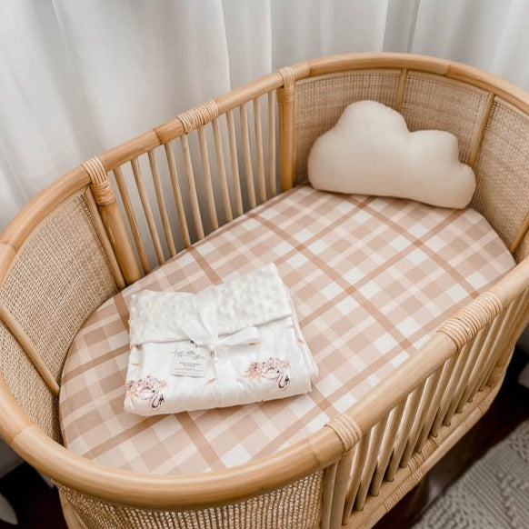 Earthy plaid bassinet sheet set in a brown cane bassinet with a cloud pillow on one side.