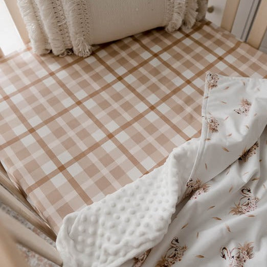 Brown plaid cotton fitted sheet depicted with a swan print dimple dot minky blanket in a light bright nursery
