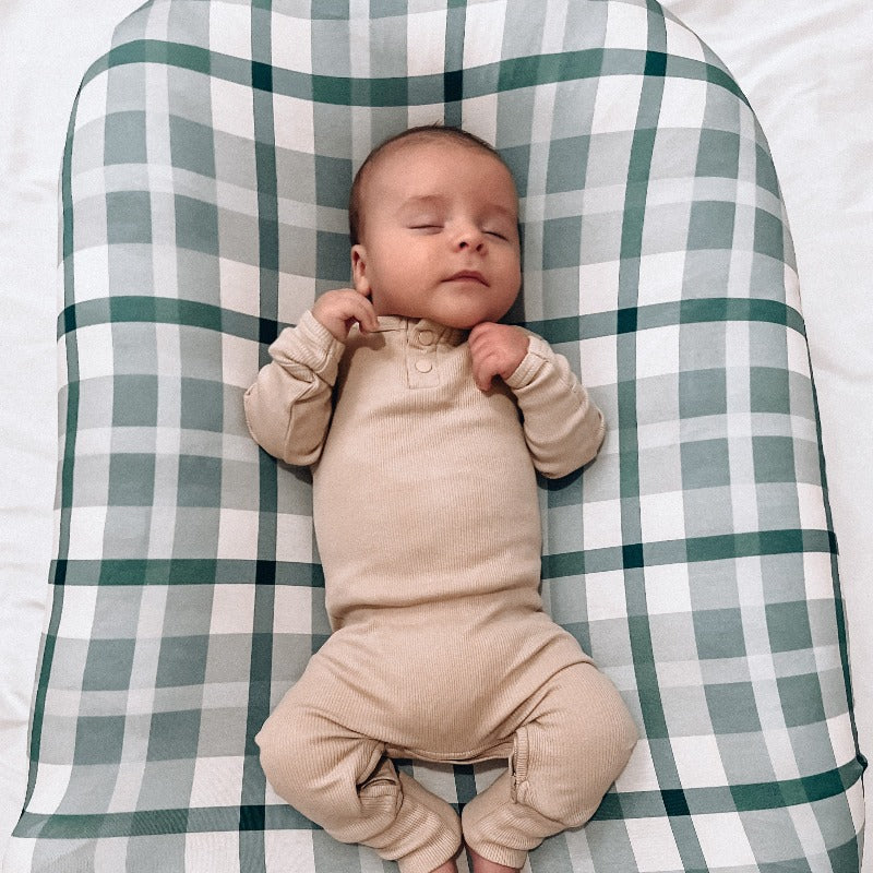 A sleeping baby using a baby lounger from snuggle me organic covered by a blue plaid change mat cover