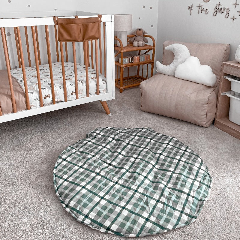 Nursery with grey carpet, pine cot with white features and a rattan bedside table showcasing the blue plaid playmat from snuggly jacks australia