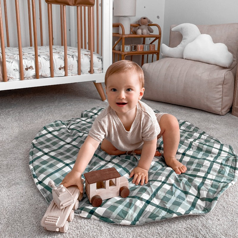 Little boy sitting on a blue cyprus plaid playmat playing with his toys in the middle a stylish nursery