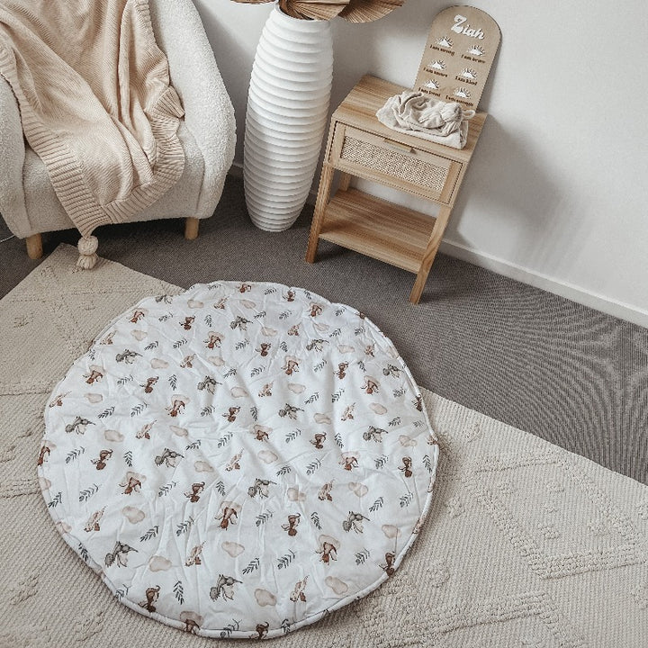 A 100% cotton playmat with adorable dragons laid out on the floor of a modern nursery with and arm chair in one corner and a pine draw with rattan details