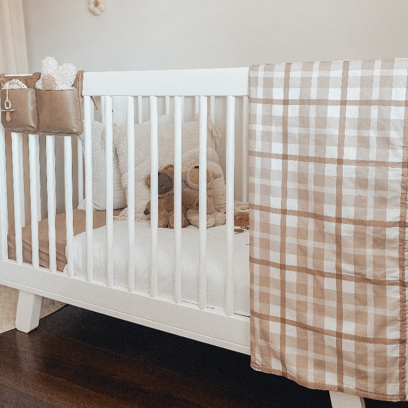 Modern nursery with a white pine cot set with solid fitted sheets and a brown plaid pram blanket thrown over the side.