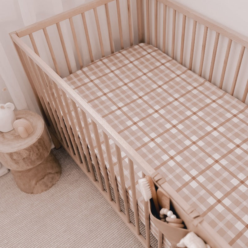 Modern nursery set including a pine cot, a bed side table made from wood and a soft brown plaid fitted sheet
