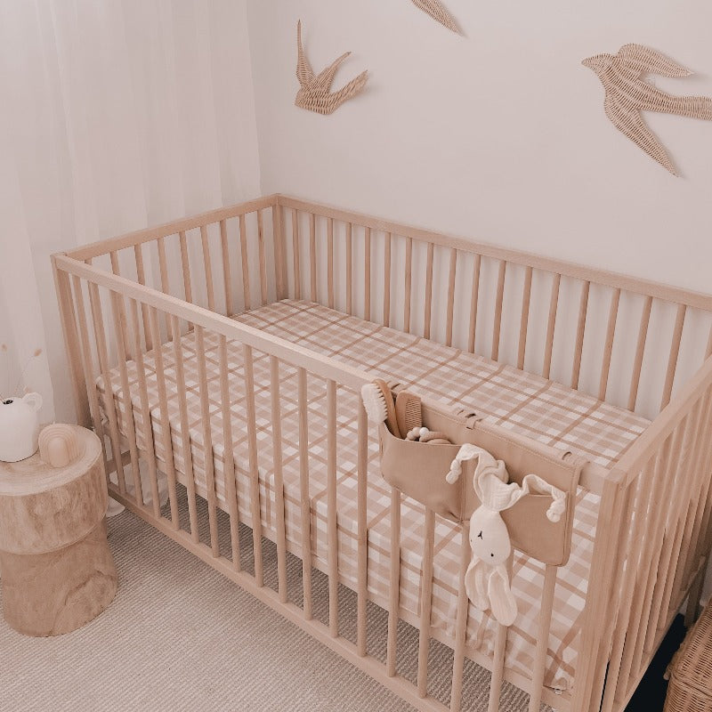 Pine cot set in the corner of a nursery with a plush bunny hanging off the front side, rattan birds on the wall and a snuggly jacks cotton fitted sheet on the mattress.