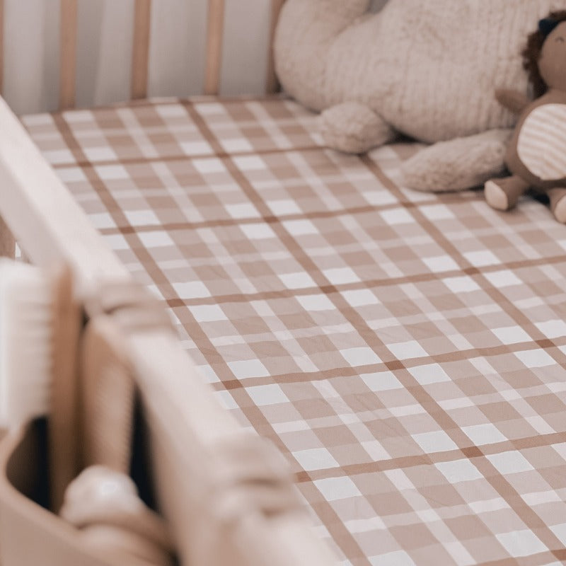 Close up of a pine cot made up using a brown plaid cotton sheet with a stuffed dinosaur and lion in the far right corner.