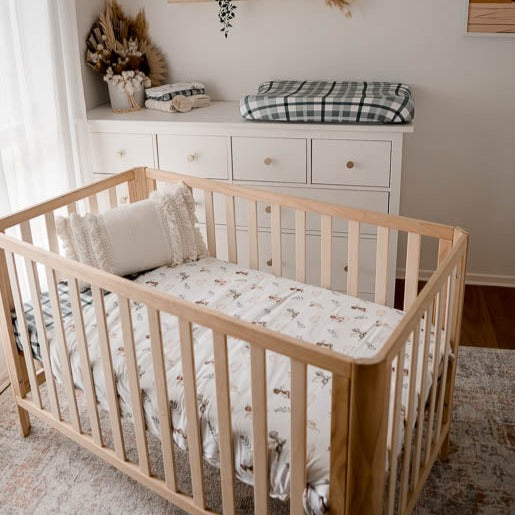 A natural pine cot set out in a modern nursery made up using blue plaid cot sheet and a cot quilt with dragon prints.