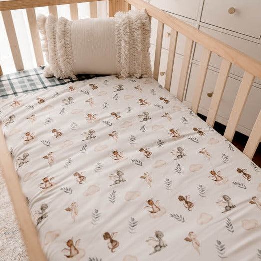 Pine cot made up with a blue plaid fitted sheet and a white cot quilt with dragons, leaves and clouds printed on it.