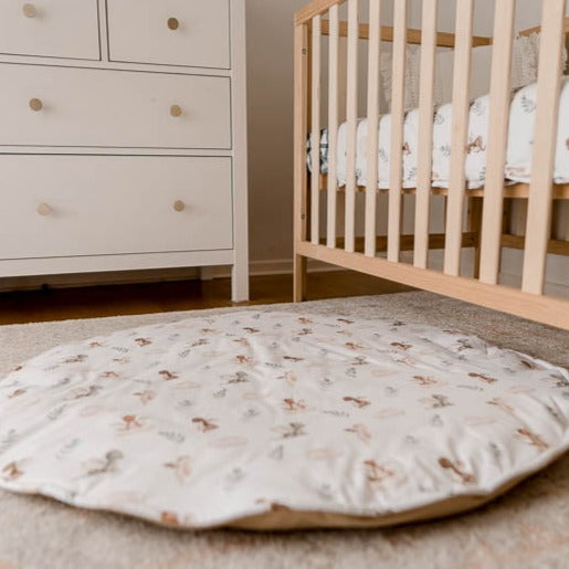 Image of a play mat with a white base and cute dragons spread out all over it set in the middle of a nursery with a white chest of draws and a pine cot
